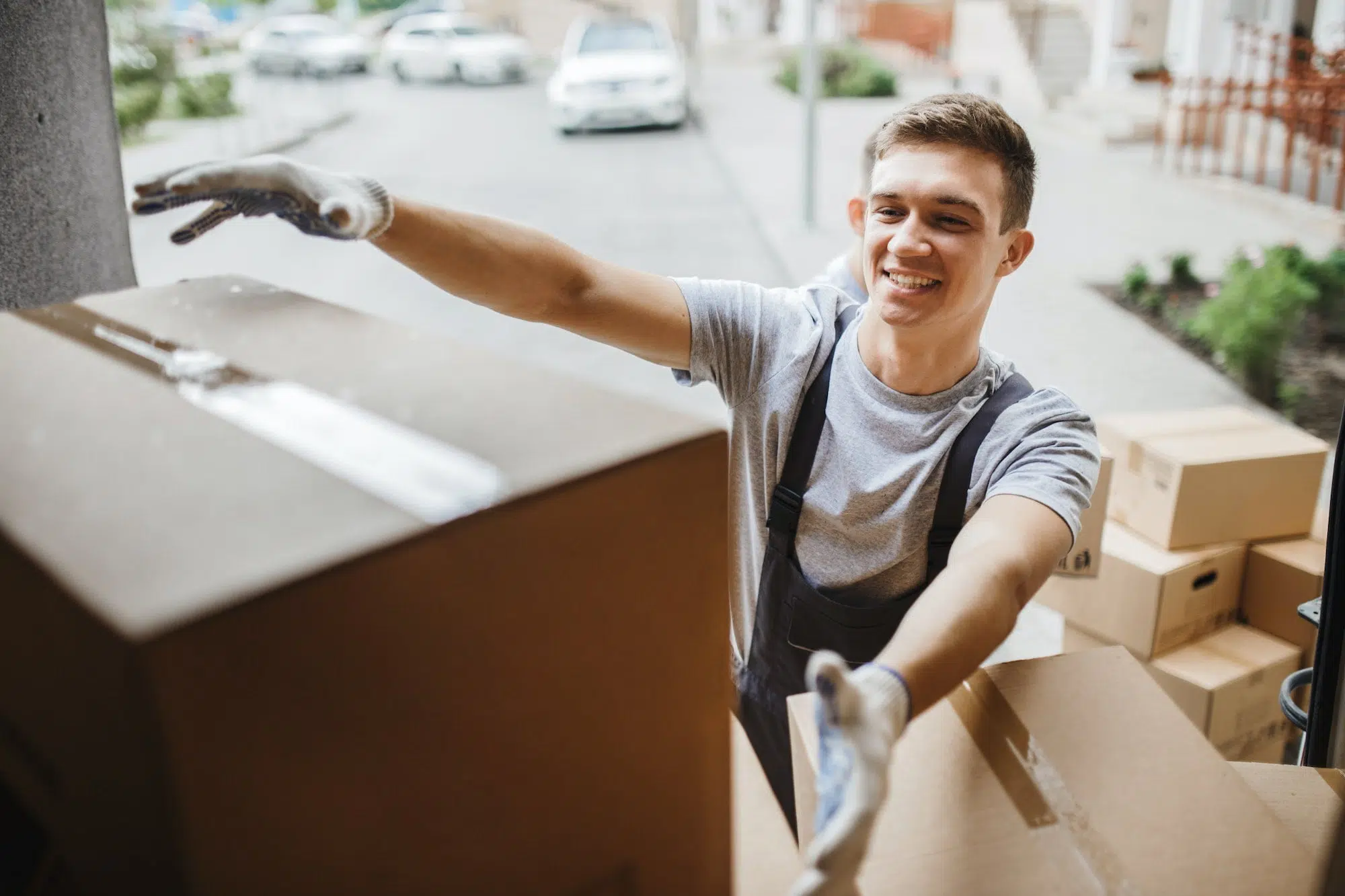 a-young-handsome-smiling-mover-wearing-uniform-is-reaching-for-the-box-while-unloading-the-van-full.jpg